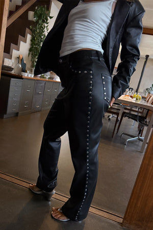 Black vegan leather trousers with silver studs along the side and pocket, styled for a London look.