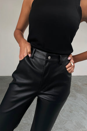 Pantaloni a vita alta in pelle vegana nera con tasche anteriori, abbinati a una canotta nera a coste.