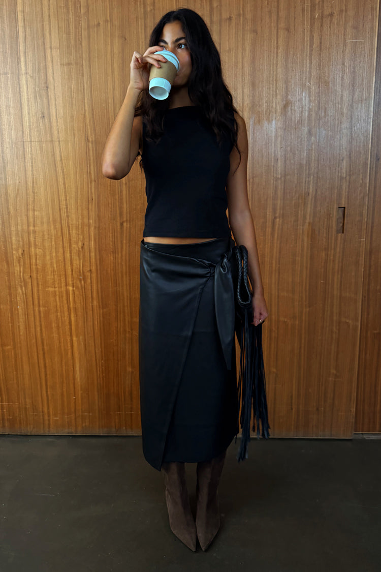 Black Vegan Leather Wrap Skirt featuring a tulip tie detail, styled with a sleeveless top and boots.