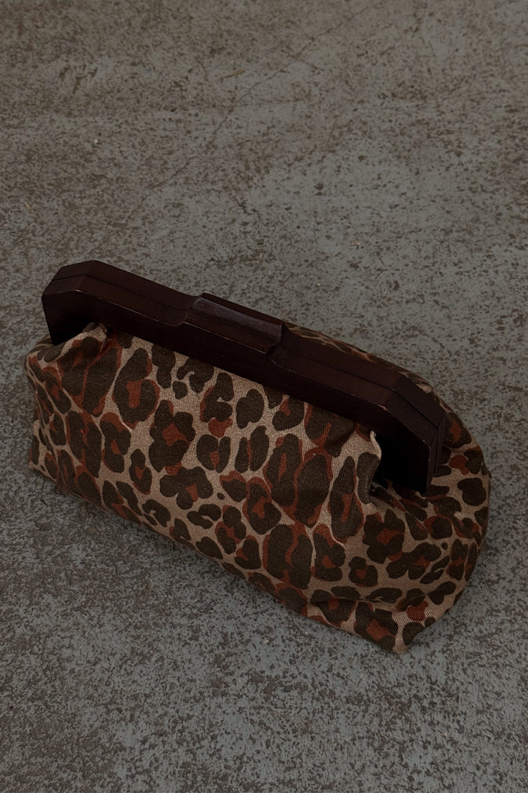 Lucia Leopard Denim Clutch Bag featuring an iconic animal print and a dark wooden handle on a textured ground.