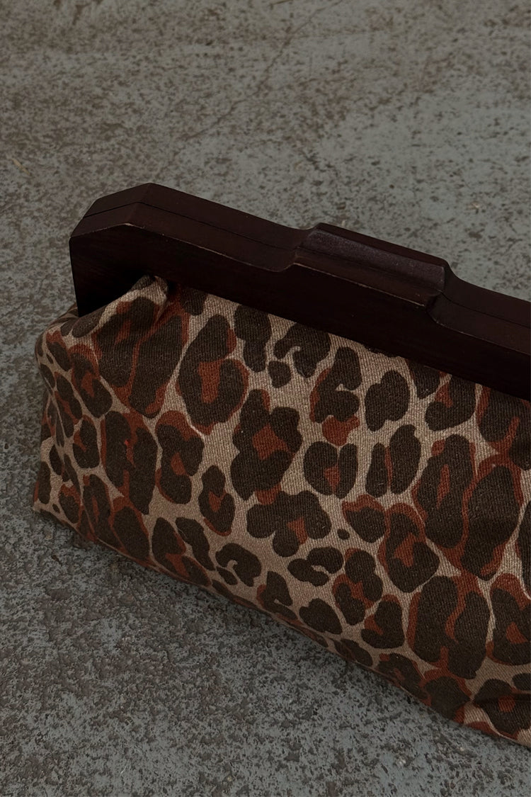 Lucia Leopard Denim Bag with a leopard print and dark wooden handle, resting on a textured surface.