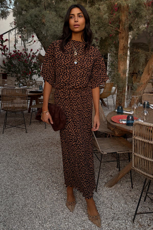 Lucia Leopard Tilly Dress Petite in iconic leopard print plisse fabric, styled with gold jewellery at an outdoor terrace.