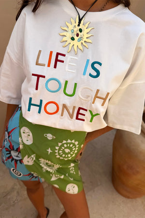 White relaxed t-shirt featuring a multi-coloured Life Is Tough Honey embroidered slogan, paired with a patterned skirt.