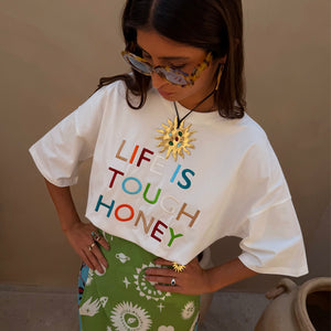 White Life Is Tough T-Shirt with colourful embroidered slogan, paired with a green patterned skirt and gold sun jewellery.
