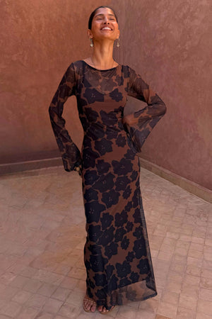 Tan Jaden Floral Mesh Maxi Dress with flared sleeves and a high neckline, worn against a terracotta background.