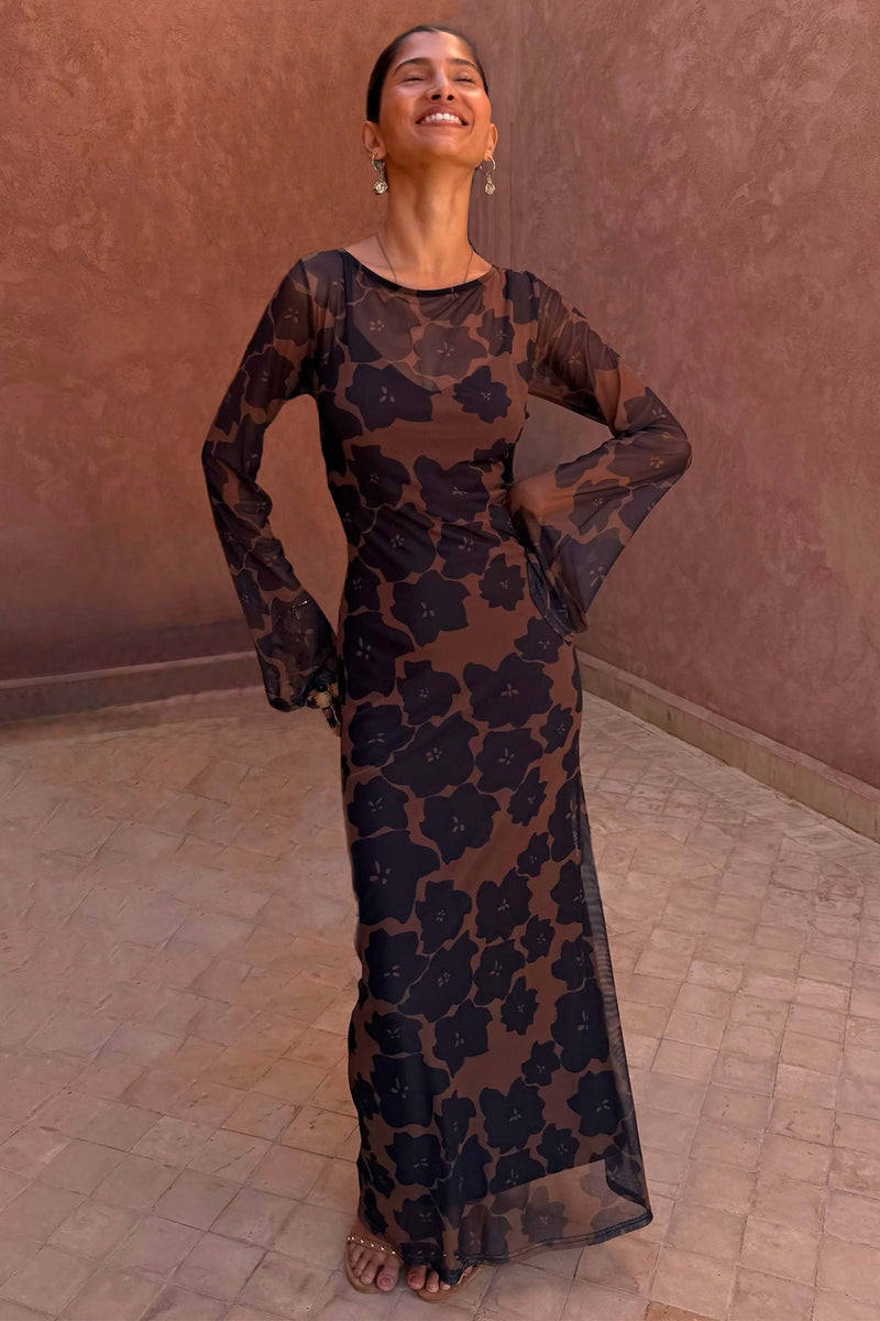 Tan Jaden Floral Mesh Maxi Dress with flared sleeves and a high neckline, worn against a terracotta background.