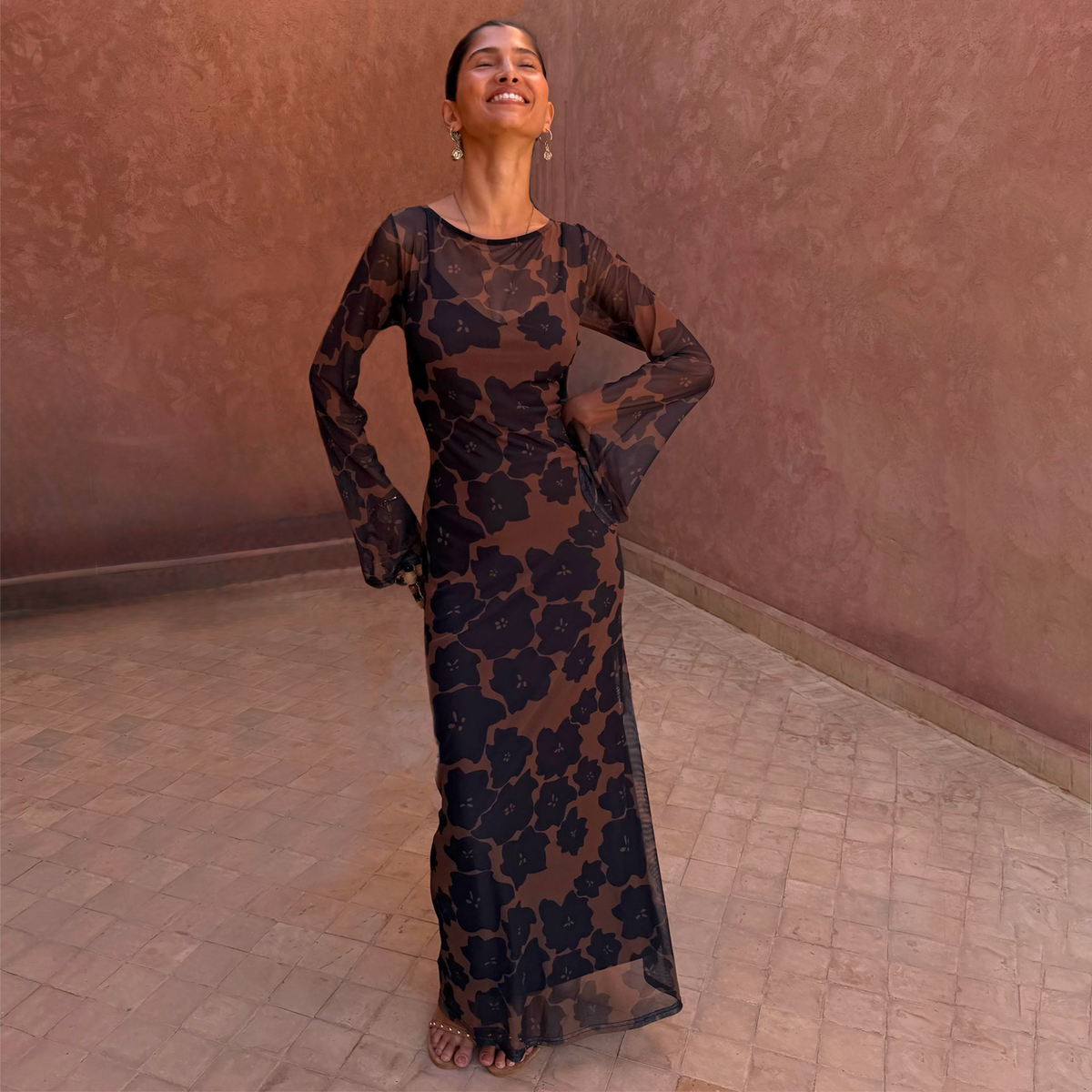 Abito maxi Tan Jaden Floral in mesh con maniche trasparenti a campana in un cortile soleggiato.