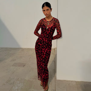 Red digital cherry print Mesh Soho Dress with long sleeves, designed in London and worn by a model against a wall.
