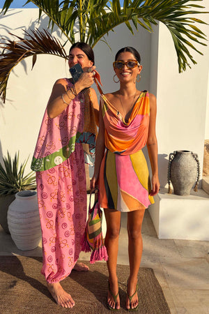 Green Abstract Leila Mini Dress with a vibrant multi-colour print and cowl neck in a sun-drenched vacation setting.