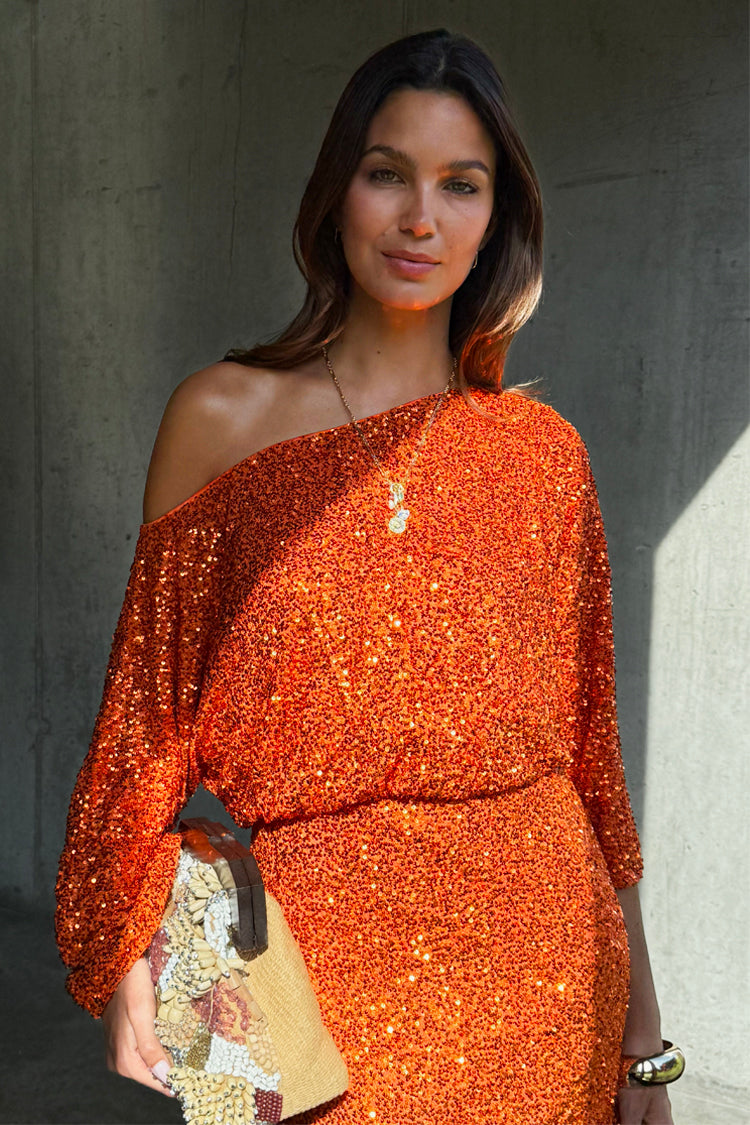 Orange Sequin Tilly Dress in an off-the-shoulder silhouette with long sleeves, paired with a beaded clutch.