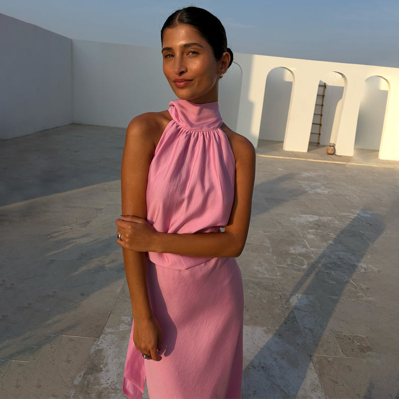 Pink Billie Top with a gathered halterneck and draped fit, styled as a co-ord against a white arched backdrop.