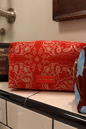 Red Bandana Reversible Make Up Bag with an in-house designed paisley print and gold zipper on a tiled shelf.