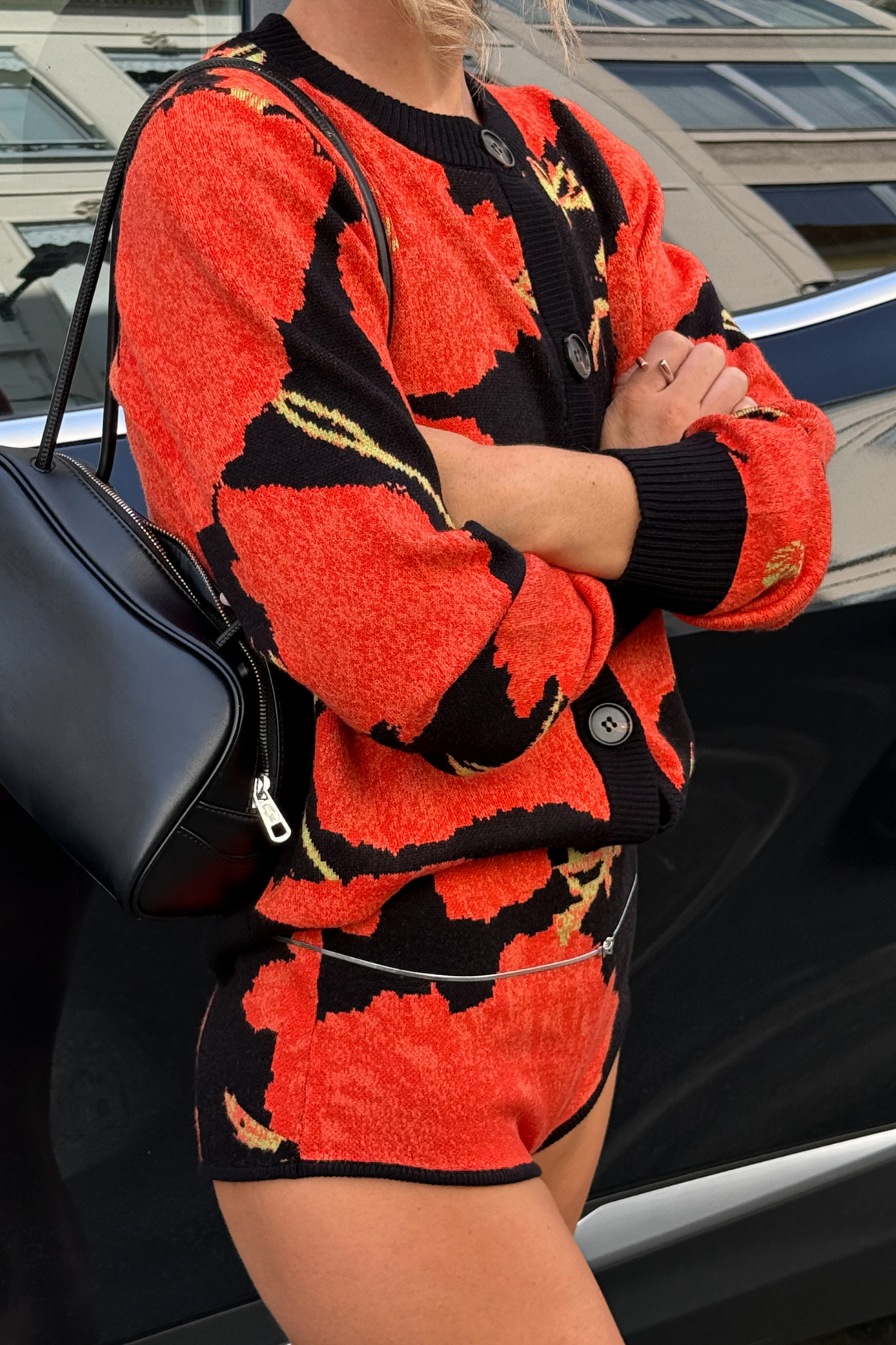 Black Poppy Cardigan with an iconic red poppy print and wide sleeves, paired with matching shorts and a black bag.