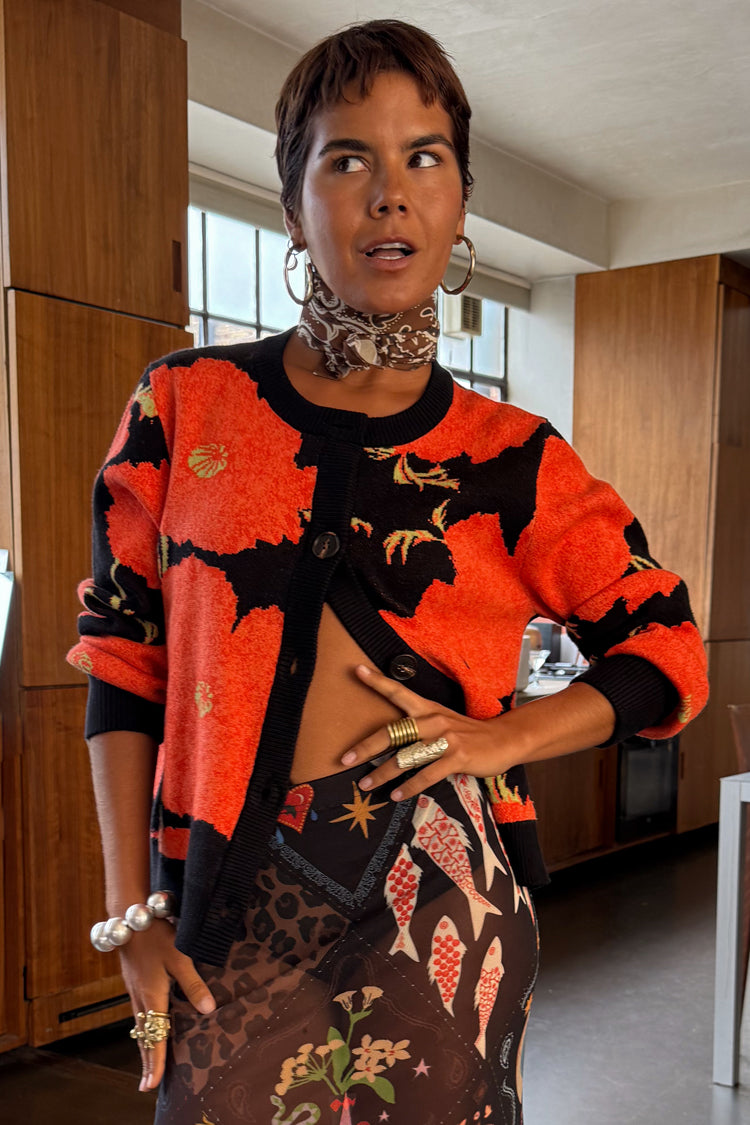 Black Poppy Cardigan with an iconic red poppy print and wide sleeves, styled over a patterned mesh dress.
