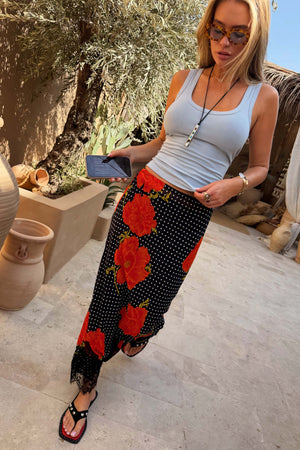 Black Poppy Midi Maeva Skirt in a red poppy and polka dot print with lace trim, styled in a sunny garden.