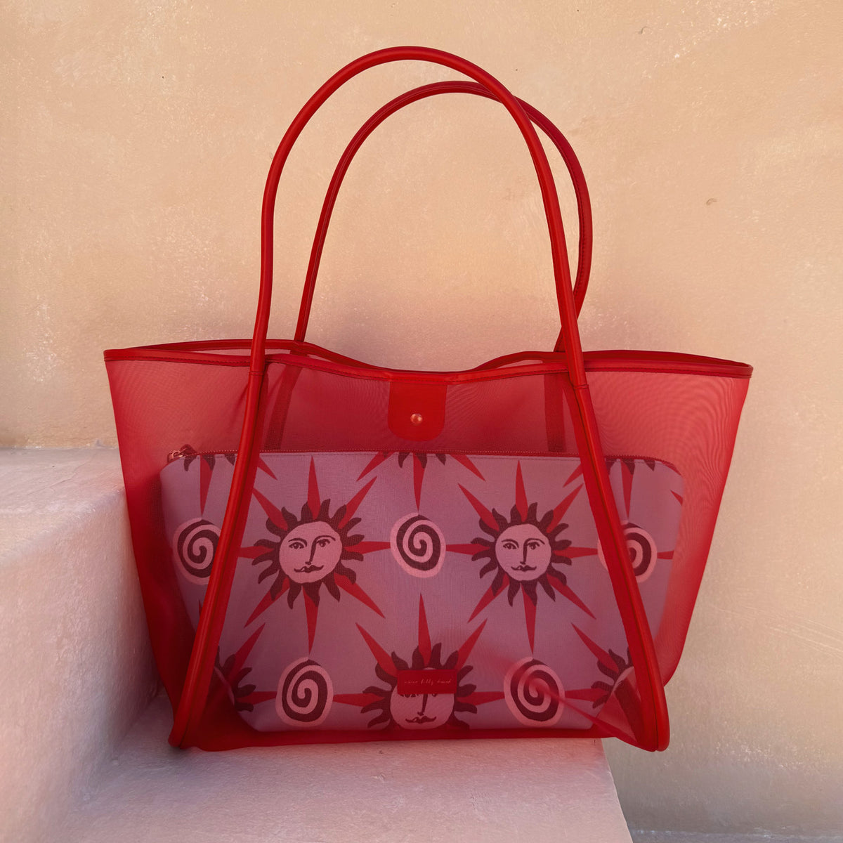 Red Mesh Tote Bag with leather straps and a sun-printed pouch, displayed on light stone steps.