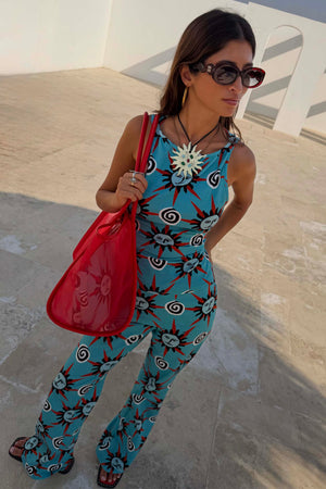 Occhiali da sole rossi con aste a zigzag in acetato indossati con borsa rossa e completo blu a stampa solare.