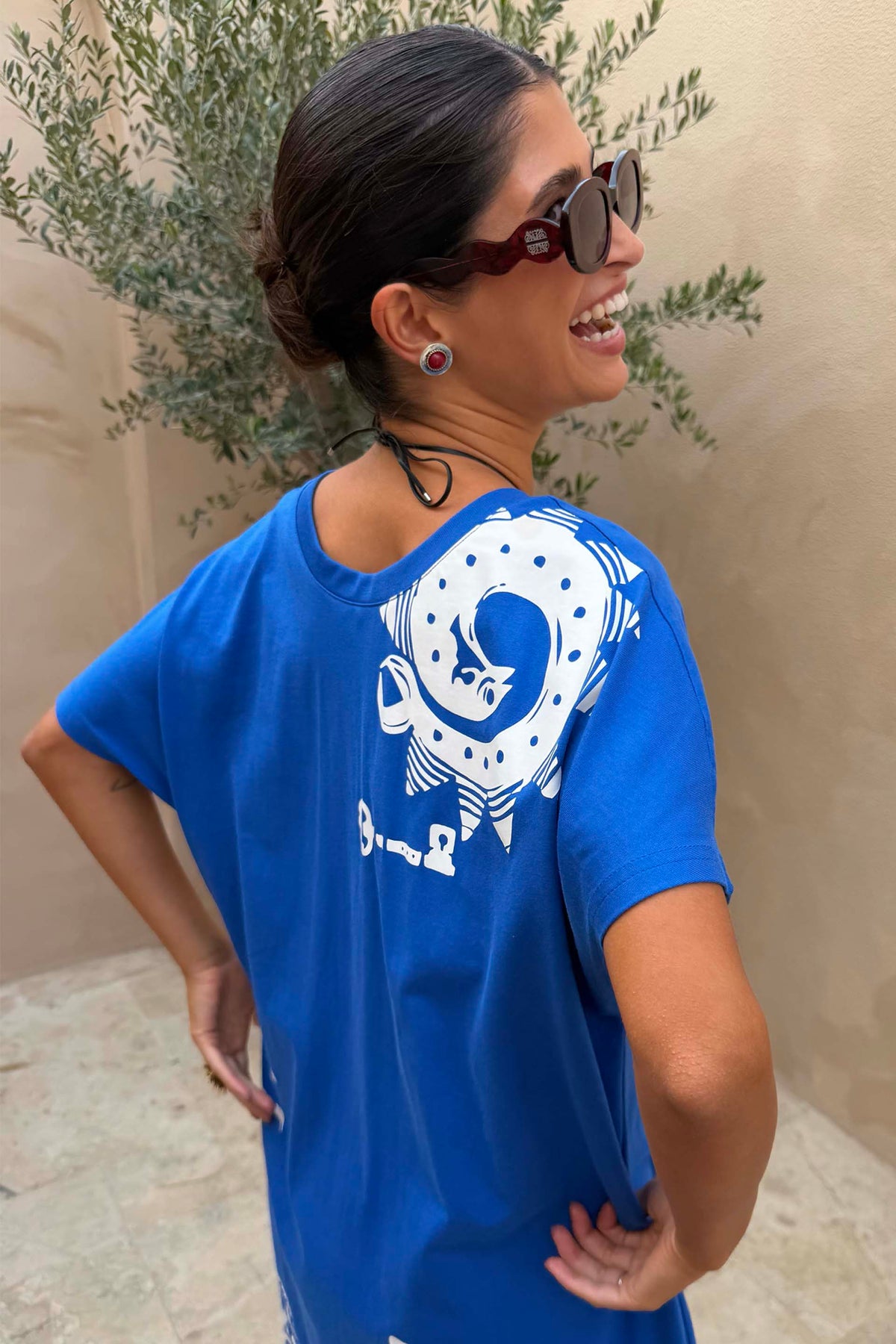 Occhiali da sole rossi Red Wiggle Arm in acetato con stanghette ondulate indossati con t-shirt blu.