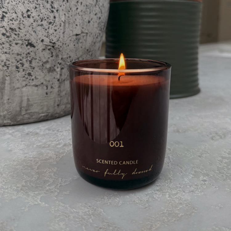 Lit NFD Scented Candle 001 in a dark amber glass jar with gold branding on a neutral stone surface.