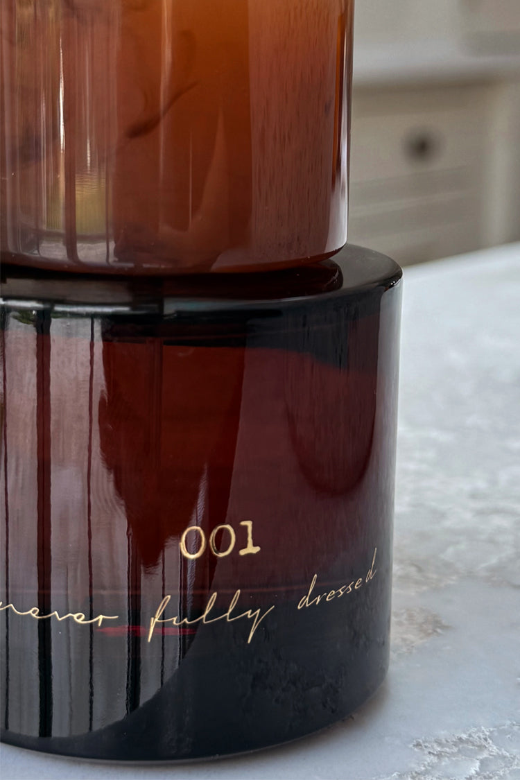 NFD Eau De Parfum 001 in an amber glass bottle featuring gold script lettering on a light stone surface.