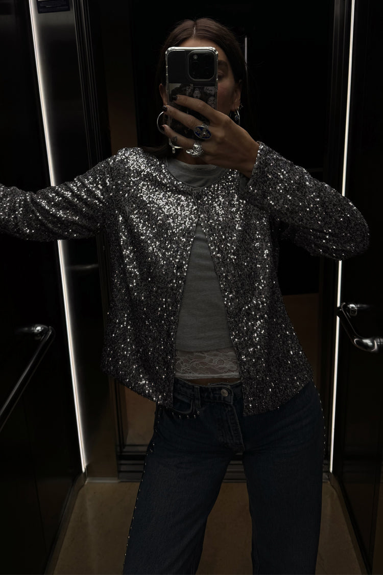 Gunmetal Alexa Sequin Cardigan in a structured silhouette, styled over a grey top and jeans for a party-ready look.
