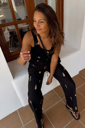 Black Shell Elissa Trousers with a gold seashell print and wide-leg fit, styled for a vacation look.