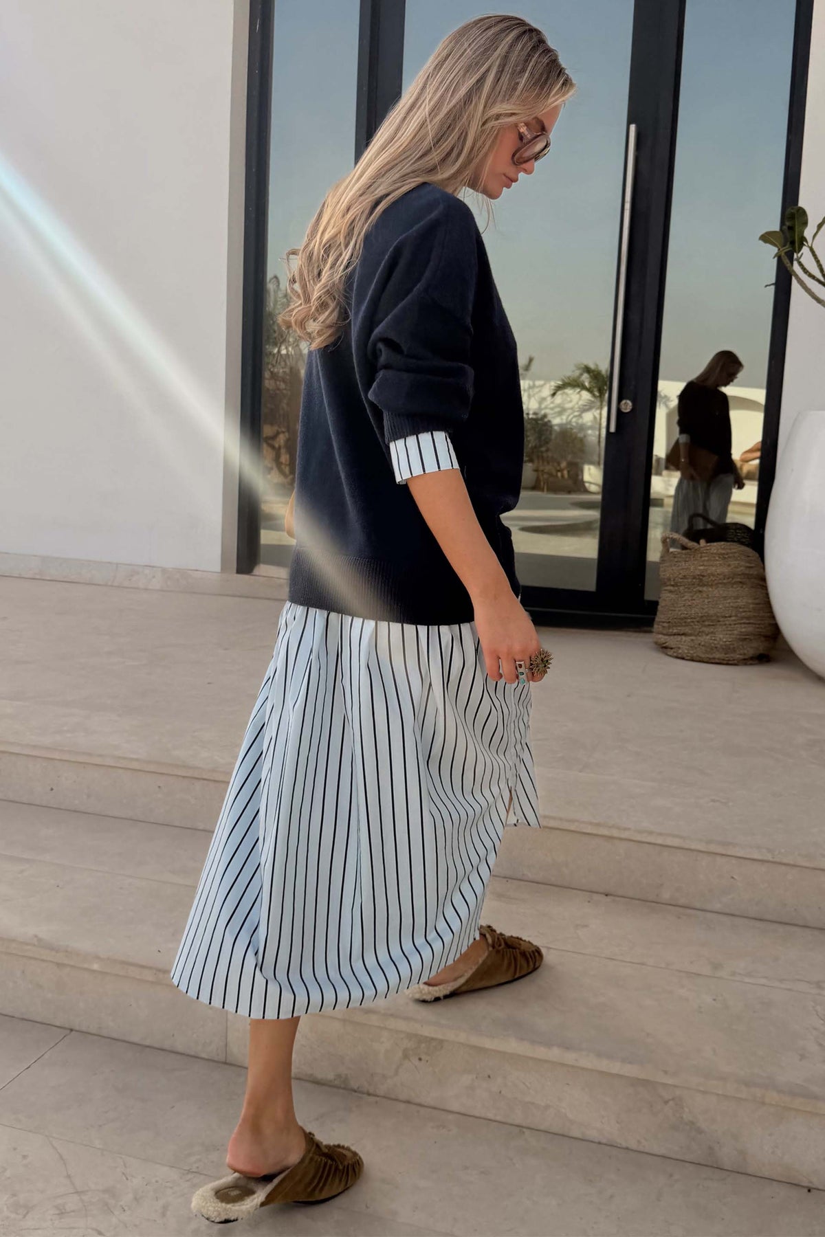 Navy Knit Jumper Dress with a blue stripe cotton skirt, designed in London and shown on a model walking outdoors.