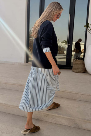 Navy Knit Jumper Dress with a blue stripe cotton skirt, designed in London and shown on a model walking outdoors.