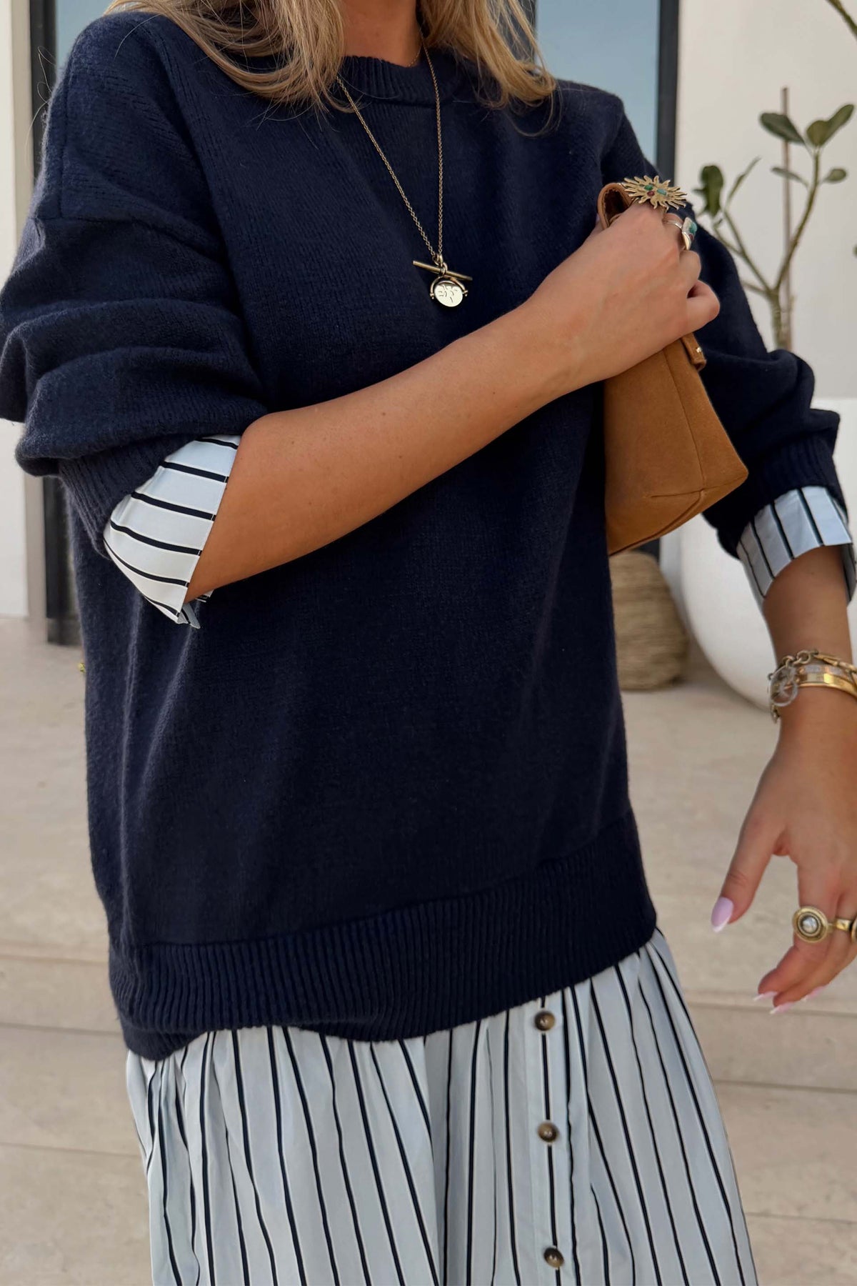 Navy knit jumper dress with a blue striped cotton skirt and layered cuffs, styled with a tan bag.