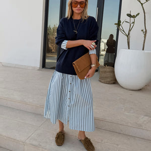 Navy Knit Jumper Dress with a blue stripe cotton skirt, styled with a tan suede clutch for a casual London look.
