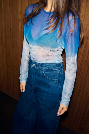 Ski Slopes Mesh Long Sleeve Top with a blue mountain landscape print and sheer finish, paired with dark denim jeans.