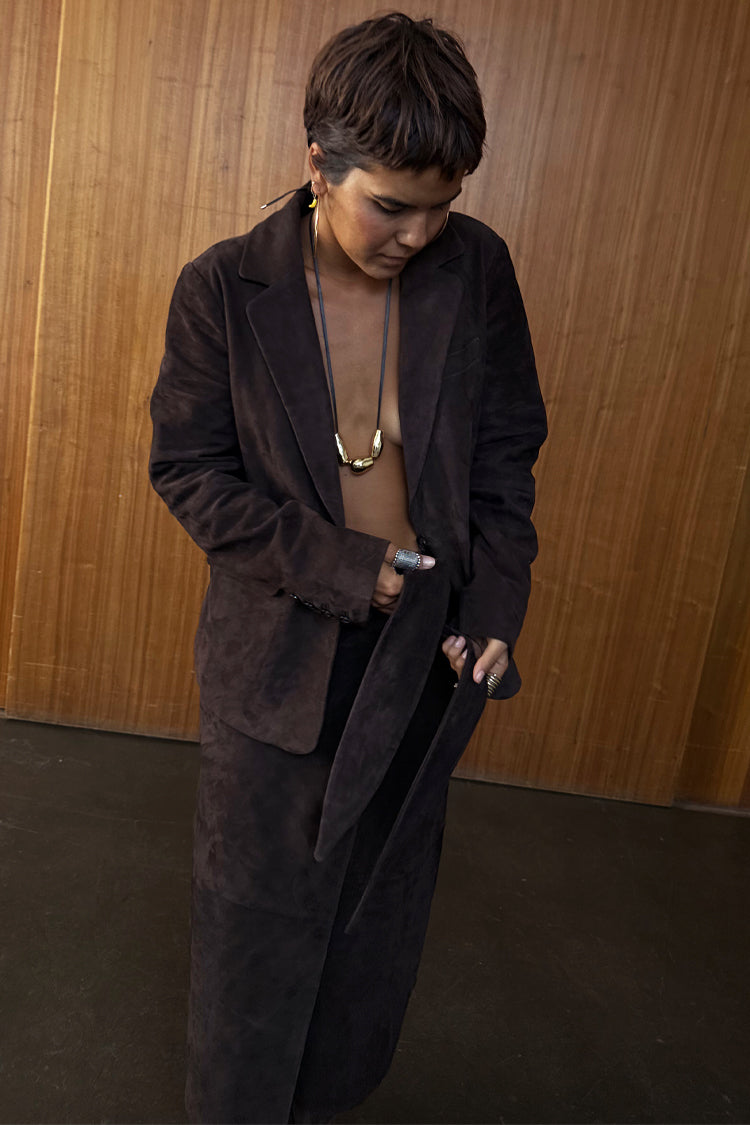 Chocolate Suede Jaspre Skirt being tied at the waist, styled with a matching blazer and gold jewellery.