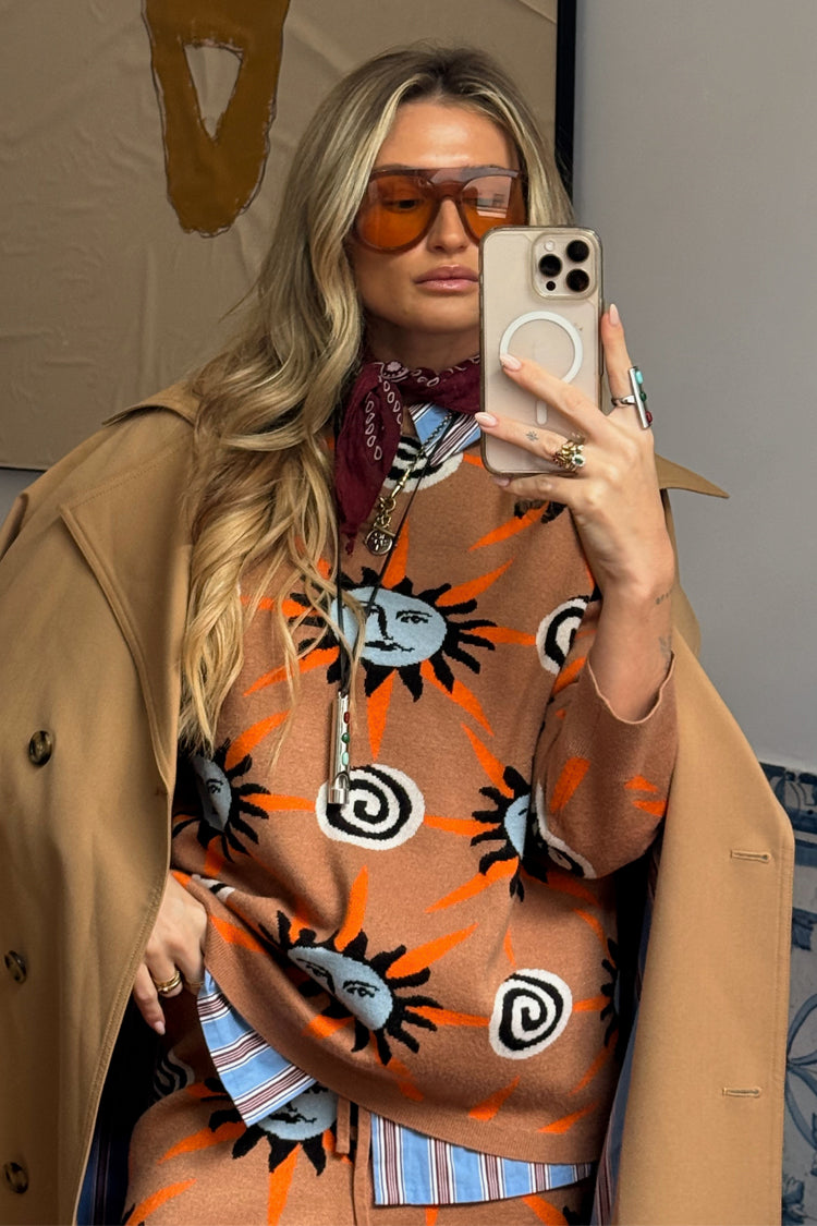 Maglione Tan Sun Copenhagen marrone con soli azzurri, abbinato a un trench e occhiali retrò in un selfie.