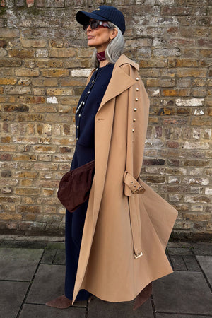 Tan Trench Coat with gold studs on the sleeve, styled with a navy cap and burgundy neck scarf.