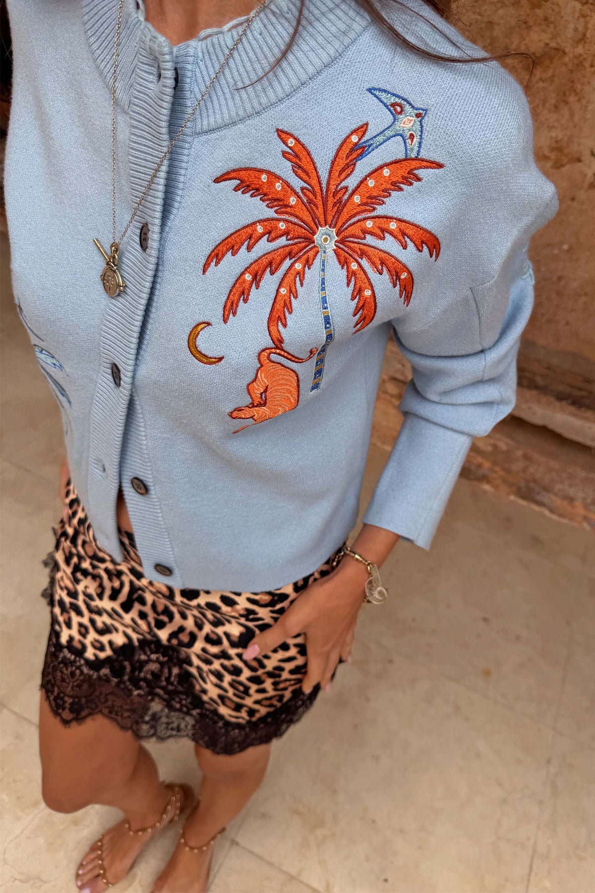 Cardigan Blue Tigress azzurro con ricamo a palma arancione, indossato con gonna leopardata rifinita in pizzo.