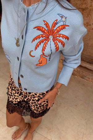 Cardigan Blue Tigress azzurro con ricamo a palma arancione, indossato con gonna leopardata rifinita in pizzo.