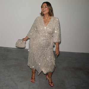 Silver Sequin Kira Wrap Dress with a multi-wear tie waist, red heels and a silver clutch bag.