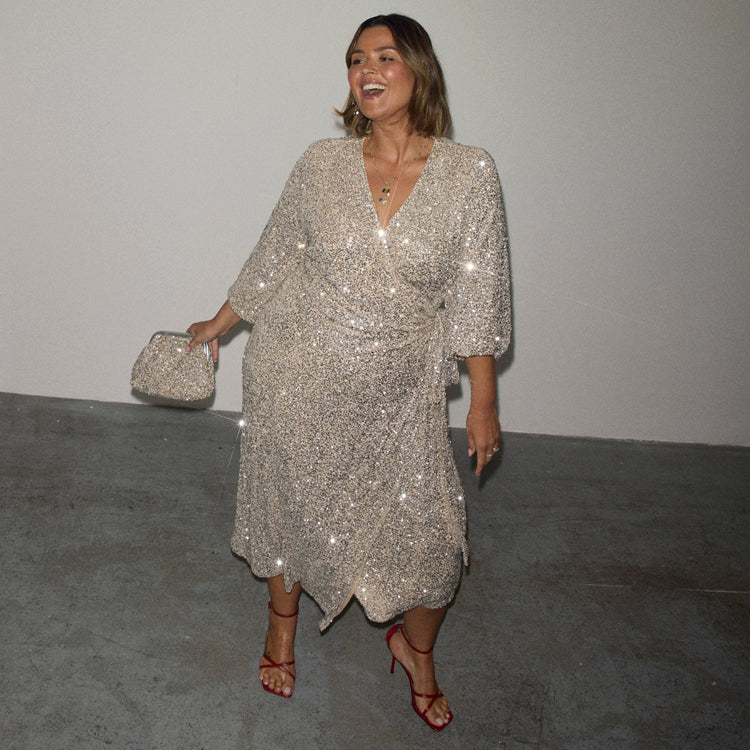 Silver Sequin Kira Wrap Dress with a multi-wear tie waist, red heels and a silver clutch bag.