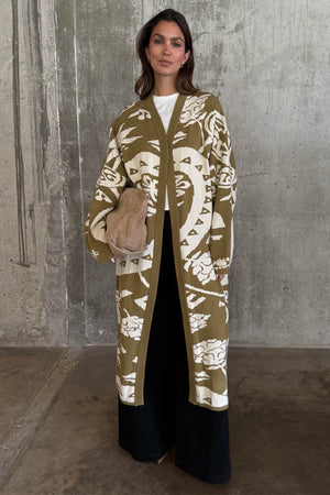 Olive Amara Knit Coatigan featuring cream eye and heart motifs, styled with black wide-leg trousers.
