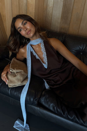 Chocolate Blue Lace Top featuring light blue lace trim and neck ties, shown on a model lounging on a leather sofa.