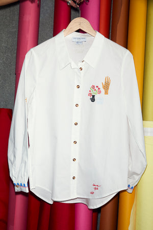 White cotton Choose Love Miley Shirt with colourful chest graphics and patterned cuffs, hanging in a studio.