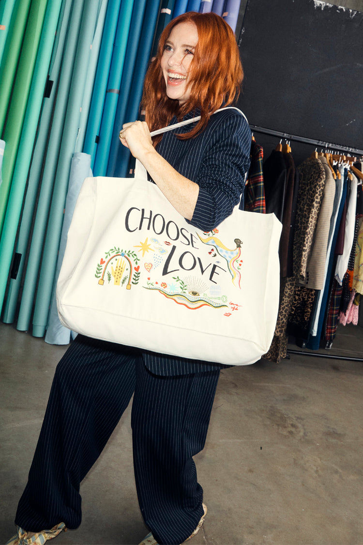 Recycled Choose Love Tote Bag in cream with colourful illustrations, carried by a woman in a pinstripe suit.
