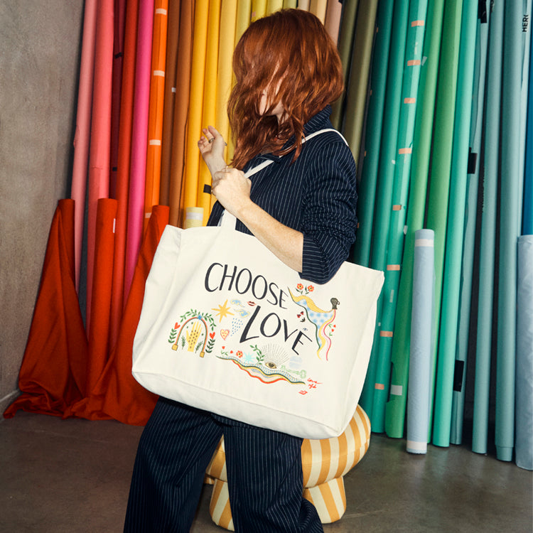 Choose Love Tote Bag in recycled cream canvas with colourful graphics, styled with a navy pinstripe suit.
