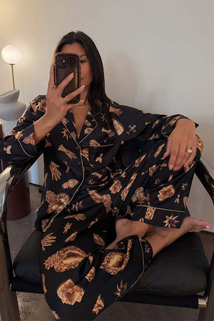 Black Deloris Button Through Pyjamas with gold hand, heart and eye motifs, worn by a model in a mirror selfie.