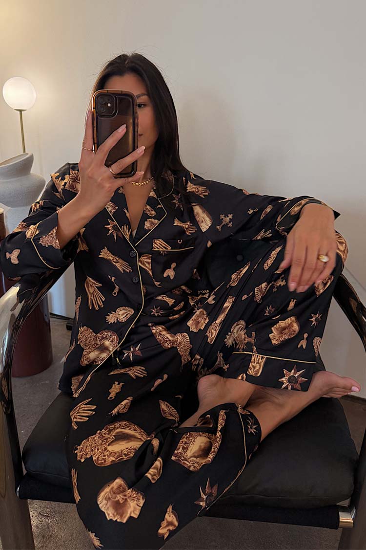 Black Deloris Button Through Pyjamas with gold hand, heart and eye motifs, worn by a model in a mirror selfie.