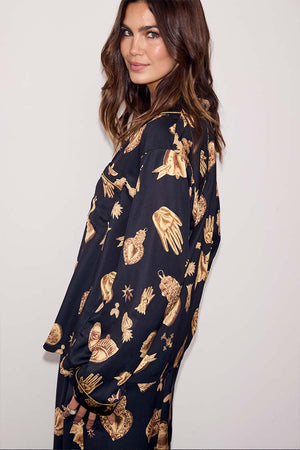 Deloris Button Through Pyjamas in black featuring gold hand and heart motifs, worn by a model looking over her shoulder.
