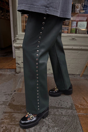 Bottle green vegan leather trousers with silver side studs, styled with chunky loafers in a street style setting.