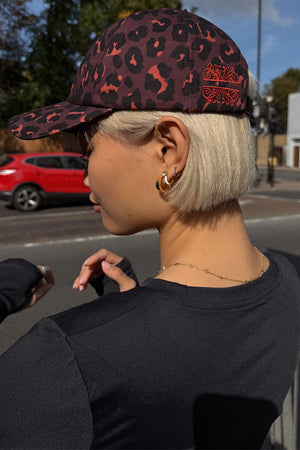 Dark Leopard Cap in iconic leopard print with burgundy tones and embroidered logo, styled on a model in a London street.