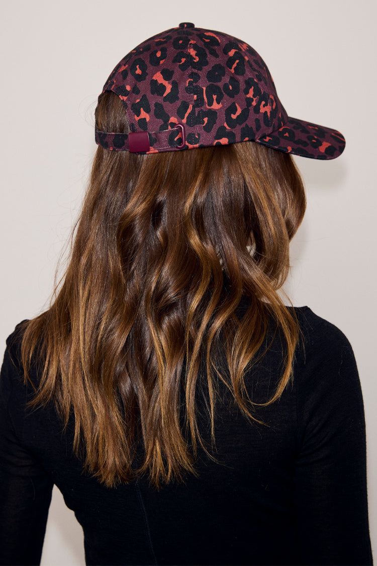 Dark Leopard Cap in iconic burgundy leopard print with adjustable back strap, shown on a model.