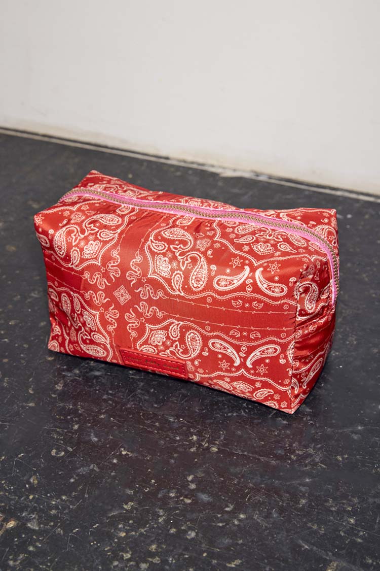 Red bandana print makeup bag featuring a reversible paisley design and pink zip closure.